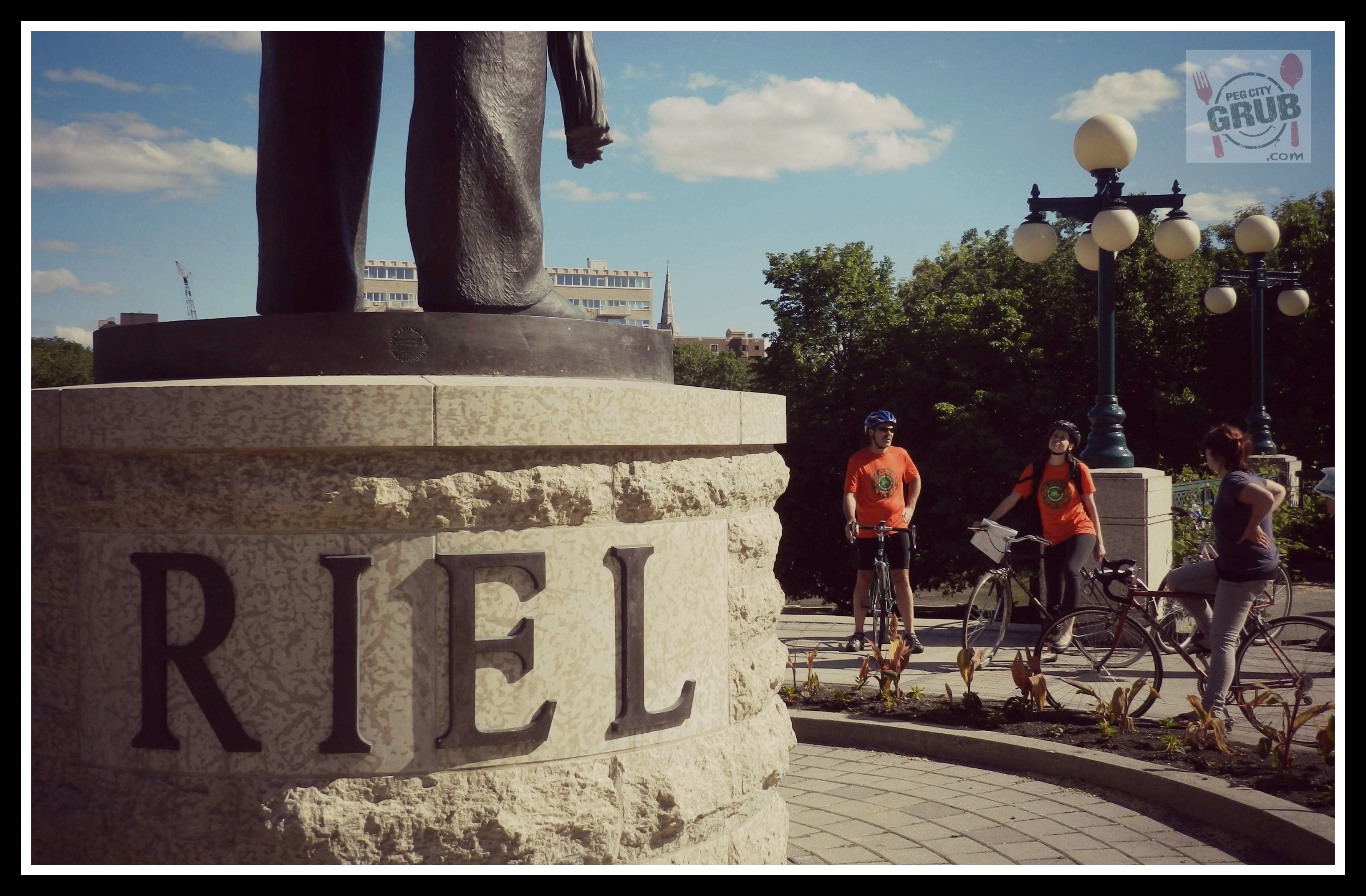 Cyclists stop at a downtown statue of Louis Riel during Moveable Feast 2013. (Photo by Robin Summerfield)